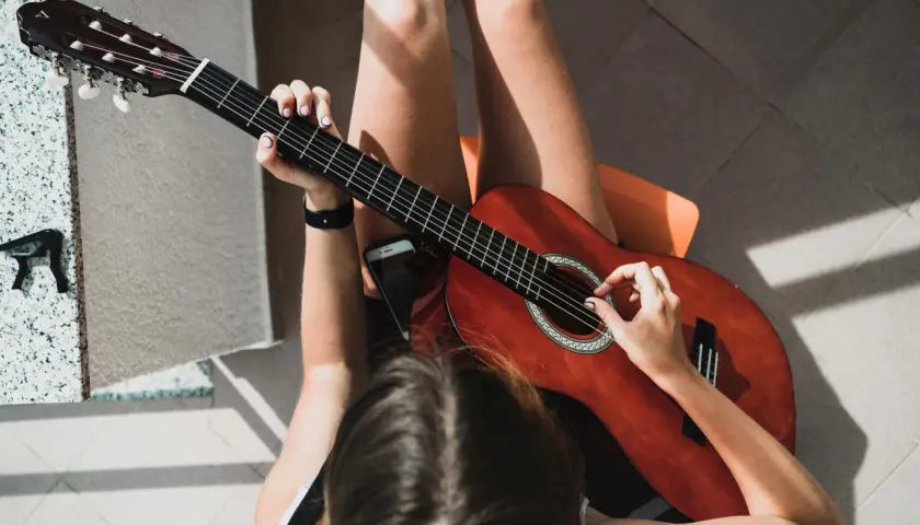 Dziewczyna gra na gitarze, jej palce tworzą akord g. Słońce rzuca ciekawe cienie.