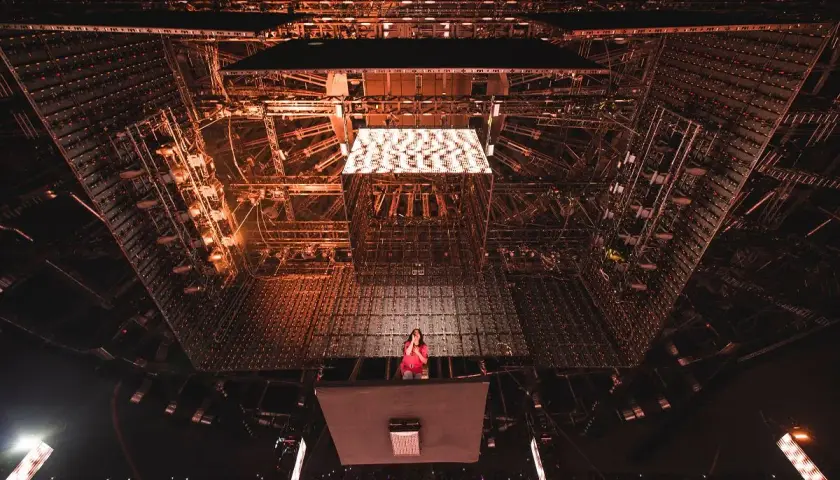 Billie Eilish na scenie, otoczona skomplikowaną konstrukcją oświetleniową. Tekst piosenki "NDA" rozbrzmiewa w tłumie.