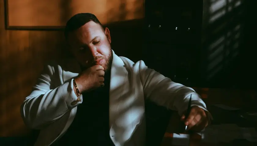 Mężczyzna w białej marynarce, Louis Villain, w zamyśleniu. Jego wiek nie jest widoczny, ale jego postawa sugeruje dojrzałość.