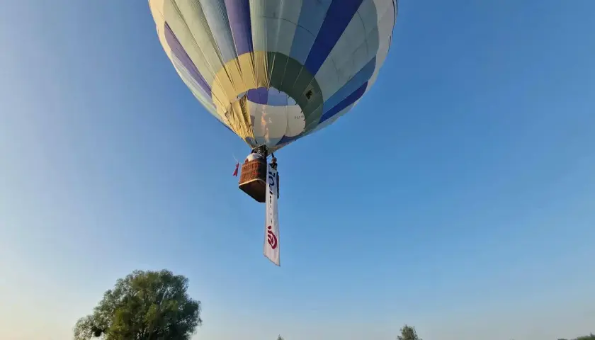 Balon z koszem i banerem unosi się na błękitnym niebie. Może to symbolizować wolność, jak w piosence "99 luftballons znaczenie".