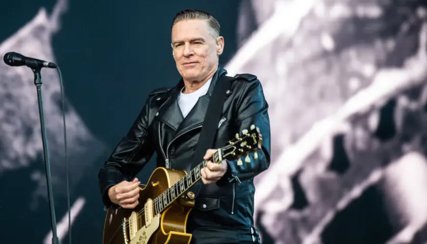 Bryan Adams w skórzanej kurtce gra na gitarze, przypominając klimat lata '69.