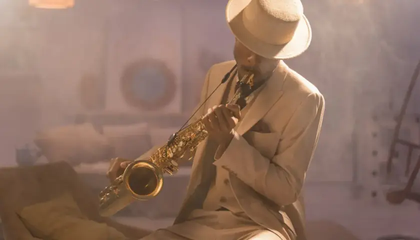 Mężczyzna w eleganckim garniturze i kapeluszu gra na saksofonie, tworząc niepowtarzalny styl w muzyce jazzowej.