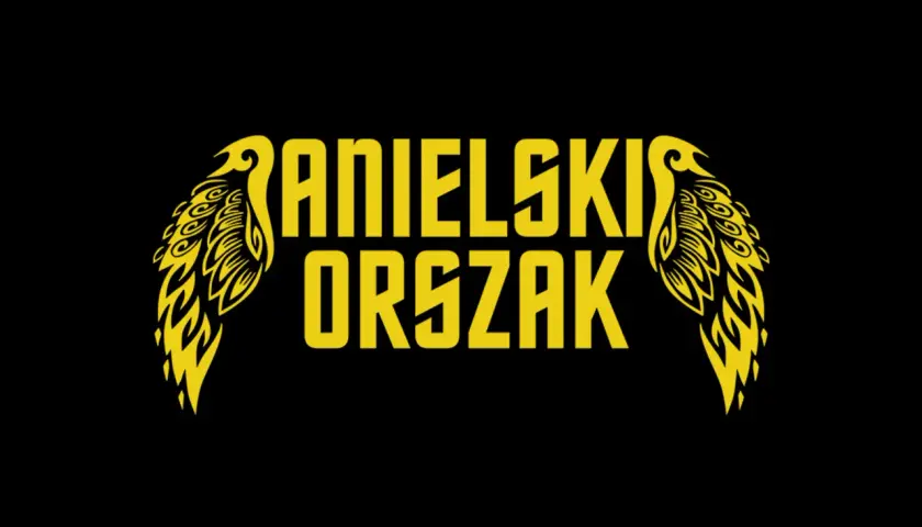 Żółty napis "ANIELSKI ORSZAK" z ozdobnymi skrzydłami po bokach, na czarnym tle.