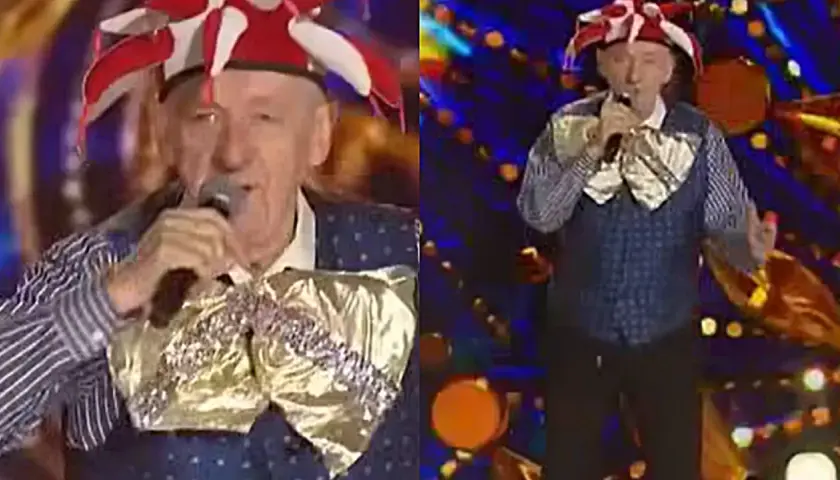 Artysta w stroju błazna śpiewa na scenie. Może to być fragment koncertu z piosenkami Rosiewicza alfabetycznie.