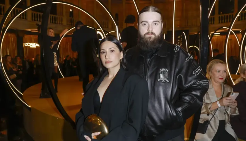 Bedoes z partnerką, która wygląda jakby była w ciąży, na złotej scenie z okręgami świetlnymi.