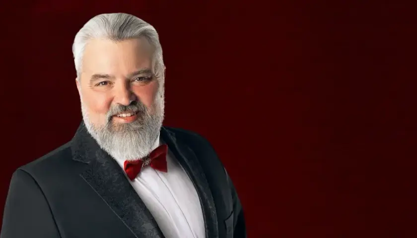 Mirosław Niewiadomski, tenor, w czarnym smokingu z czerwoną muszką, uśmiecha się do widza.