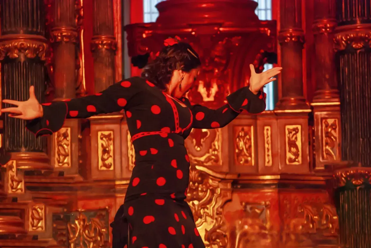 Tancerka flamenco w czarnej sukience w czerwone grochy, pełna **allegria**, porusza się na tle bogato zdobionej, złotej sceny.