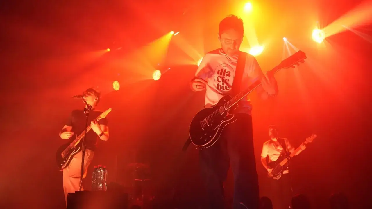 Koncert Myslovitz. Wokalista i gitarzysta na scenie, w tle basista. Czerwone światła podkreślają energię utworów.
