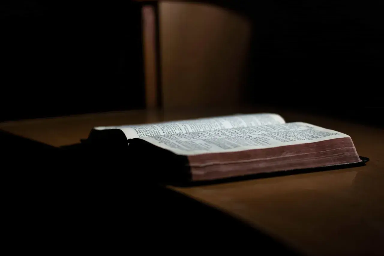 Otwarta Biblia na drewnianym stole, światło pada na strony. Słowa mądrości trwają, dopóki ziemia kręci się.