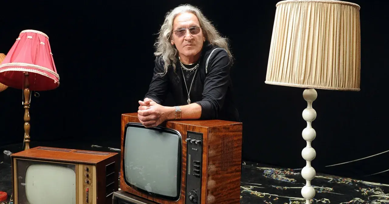 Mężczyzna z długimi siwymi włosami i okularami opiera się o stary telewizor. Wokół niego lampy i inne telewizory. Widać, że trzeba wiedzieć, kiedy ze sceny zejść.