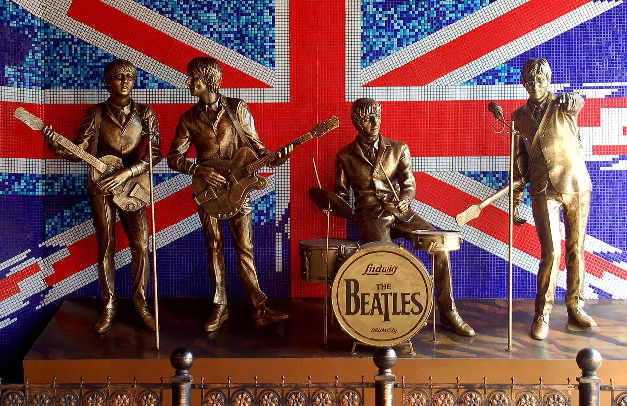 Brązowe posągi **The Beatles** grające na tle mozaikowej flagi Wielkiej Brytanii.