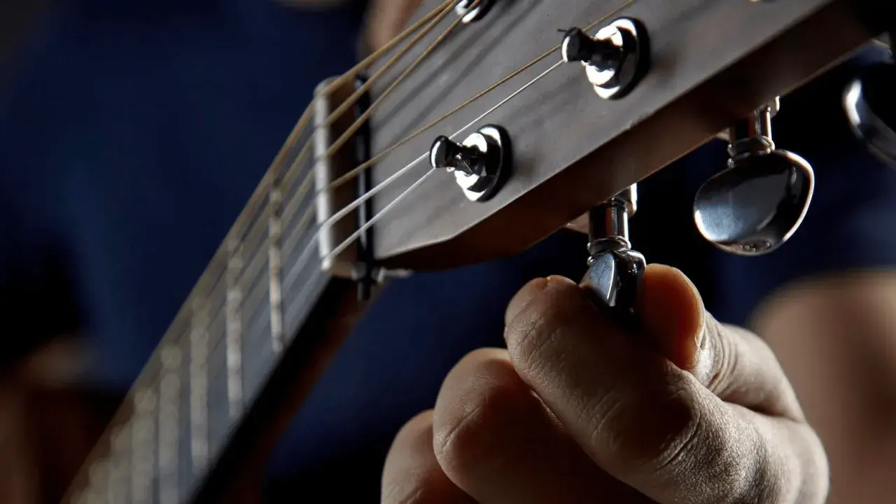 Dłoń kręci kluczem, by drop a tuning na gitarze. Idealne brzmienie jest blisko.