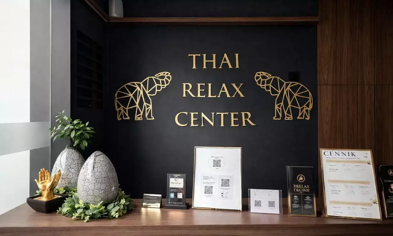 Recepcja centrum masażu tajskiego. Złote słonie i napis "THAI RELAX CENTER" na czarnej ścianie. Na blacie dekoracje i cennik. Tu możesz się wyciszyć.