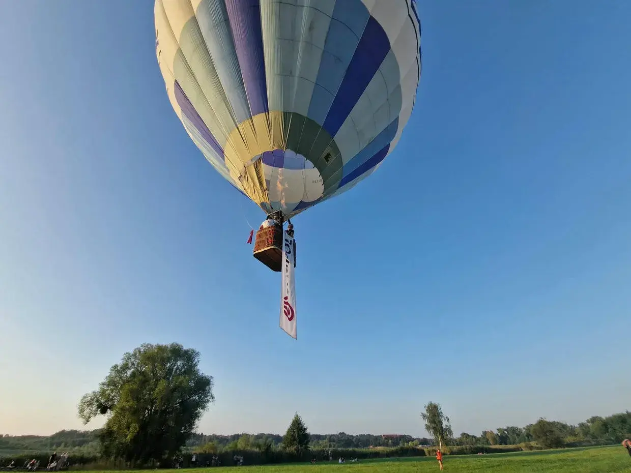 Balon z koszem i banerem unosi się na błękitnym niebie. Może to symbolizować wolność, jak w piosence "99 luftballons znaczenie".