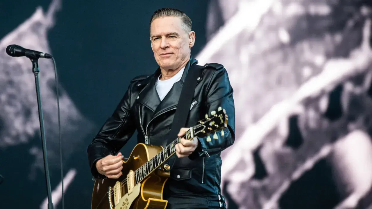 Bryan Adams w skórzanej kurtce gra na gitarze, przypominając klimat lata '69.