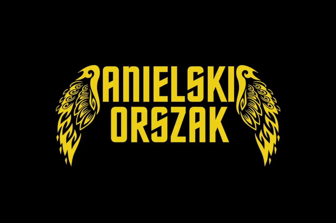 Żółty napis "ANIELSKI ORSZAK" z ozdobnymi skrzydłami po bokach, na czarnym tle.
