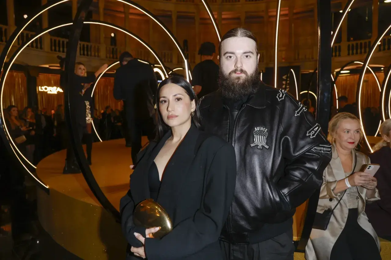 Bedoes z partnerką, która wygląda jakby była w ciąży, na złotej scenie z okręgami świetlnymi.