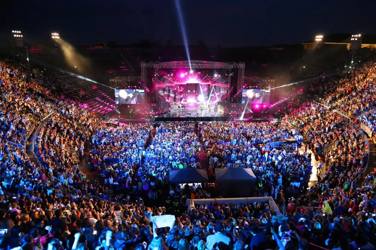 Koncert włoskich piosenkarzy na wypełnionym po brzegi stadionie. Tłum w euforii, światła sceny i ekranów tworzą magiczną atmosferę.