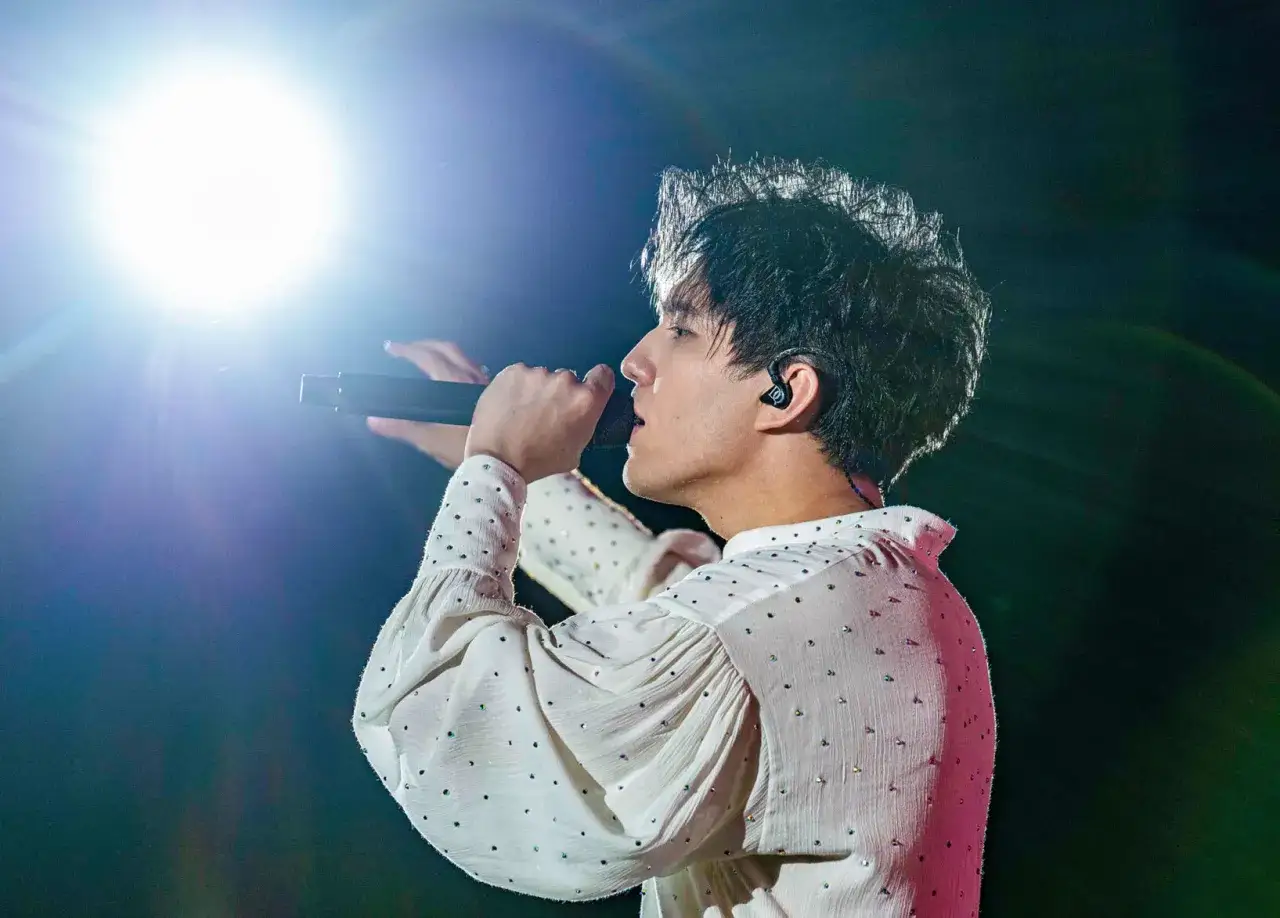 Dimash Kudaibergen na scenie, w białej, zdobionej koszuli, śpiewa do mikrofonu. Jego życie prywatne pozostaje tajemnicą, ale jego talent jest widoczny.