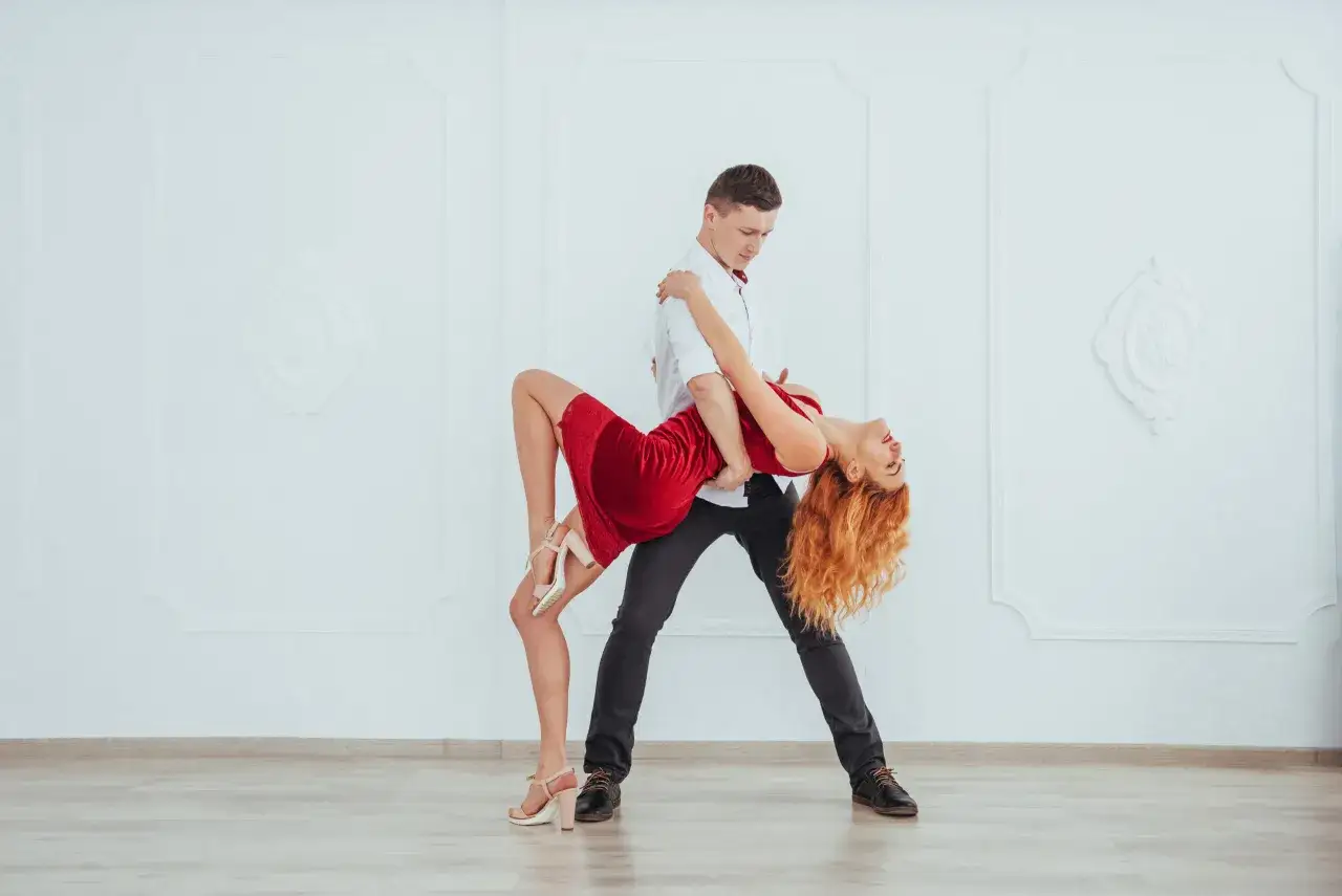 Para tańczy cha cha w rytm muzyki. Kobieta w czerwonej sukience i mężczyzna w białej koszuli wykonują skomplikowaną figurę taneczną.