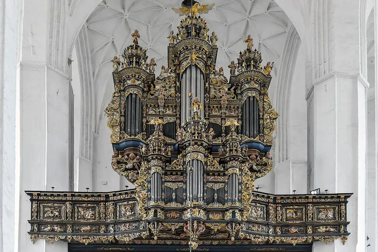Majestatyczne organy w kościele, gotowe do wygrywania wzniosłej muzyki religijnej. Złote zdobienia i rzeźby aniołów dodają im blasku.