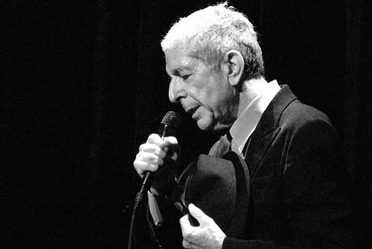 Leonard Cohen śpiewa swoje ponadczasowe utwory, trzymając mikrofon i kapelusz.