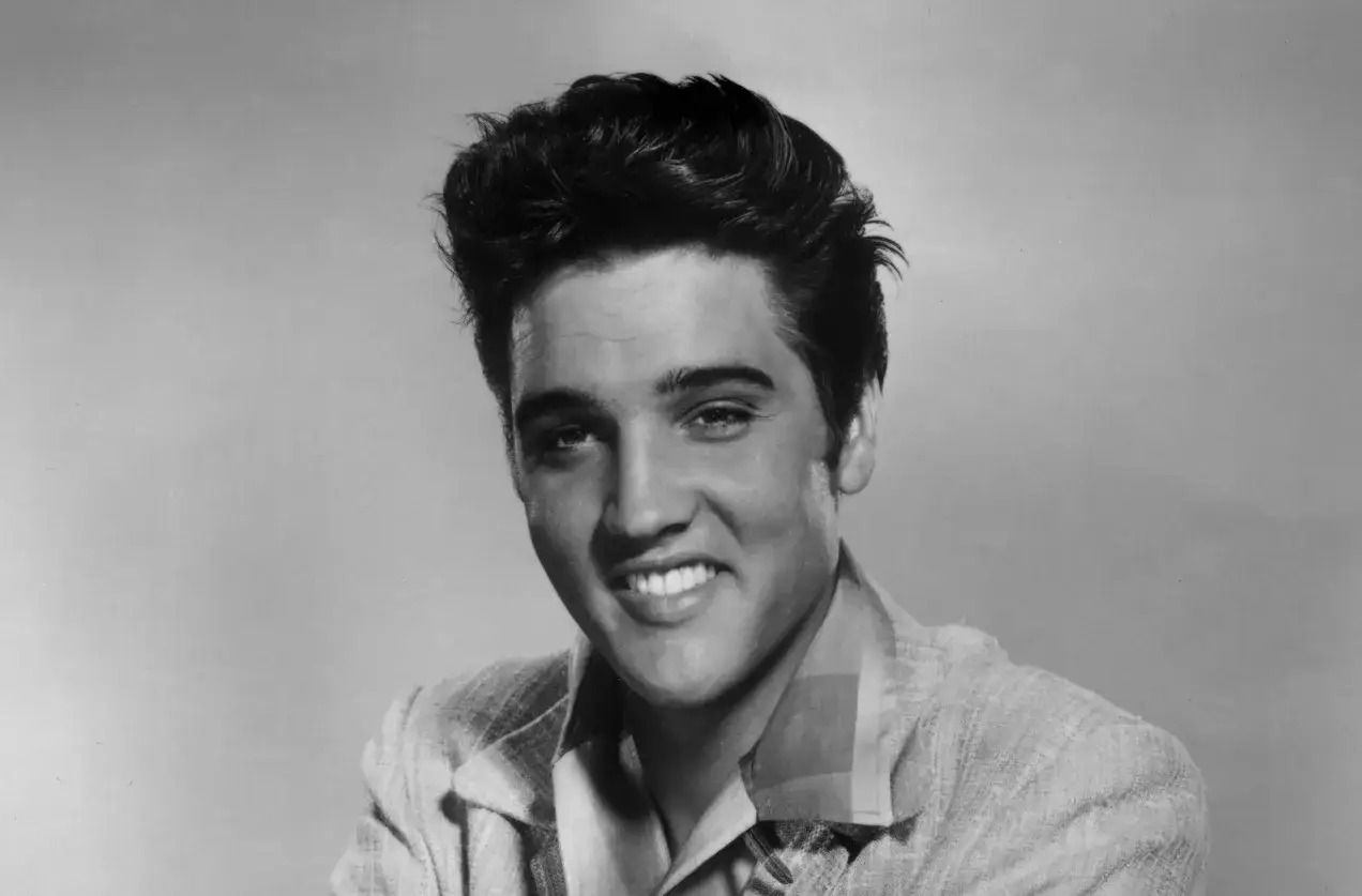 Młody Elvis Presley, uśmiechnięty, w marynarce. Słuchając 