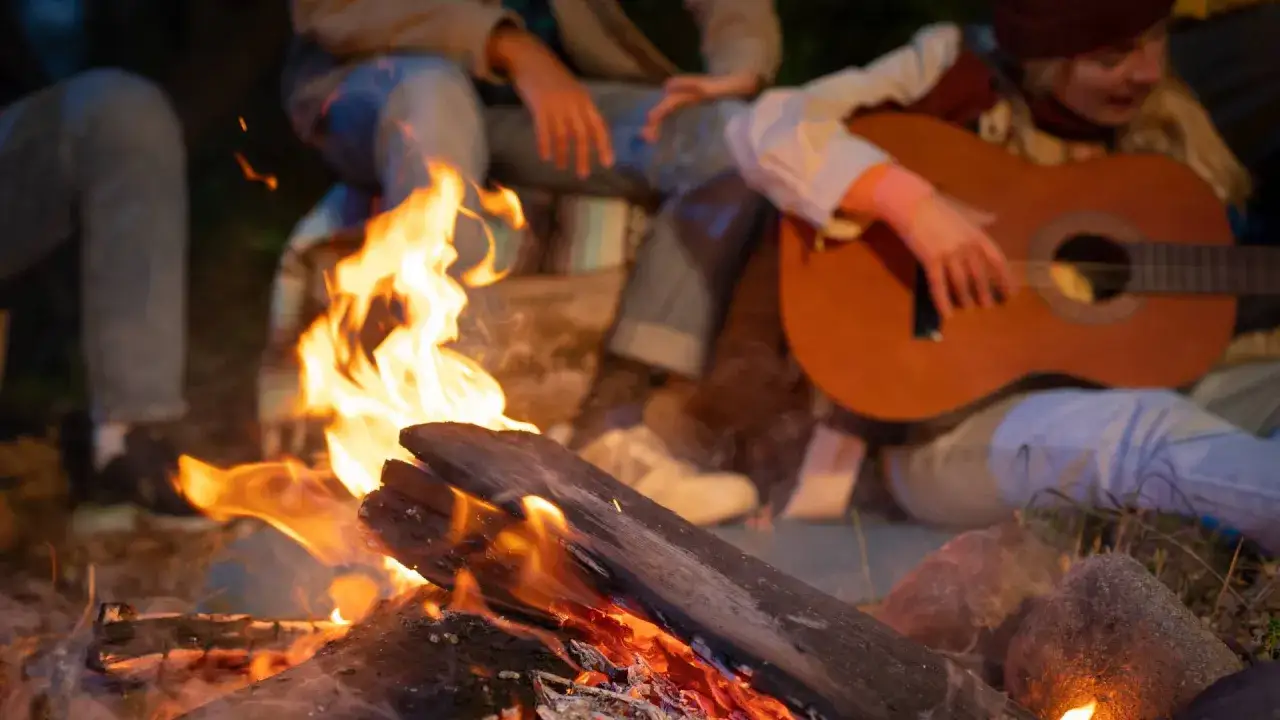 Przy ognisku, przyjaciele śpiewają fajne piosenki do śpiewania, jeden z nich gra na gitarze.
