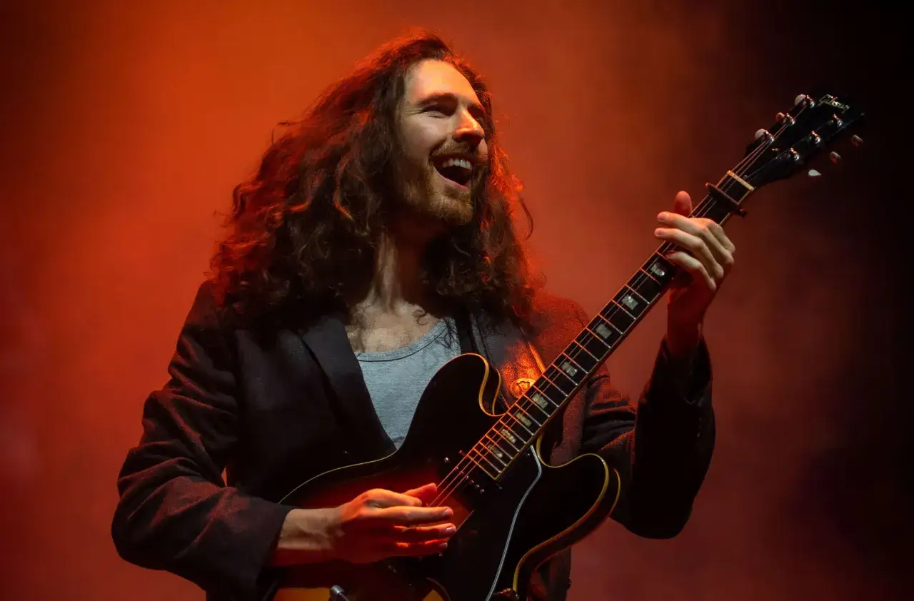 Hozier śpiewa i gra na gitarze, a jego uśmiech pasuje do tekstu 