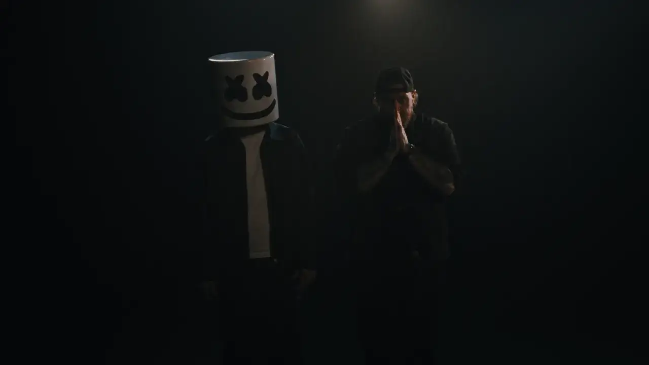 Dwóch mężczyzn w mroku. Jeden w masce Marshmello, drugi z dłońmi złożonymi do modlitwy. Panuje absolutna cisza.