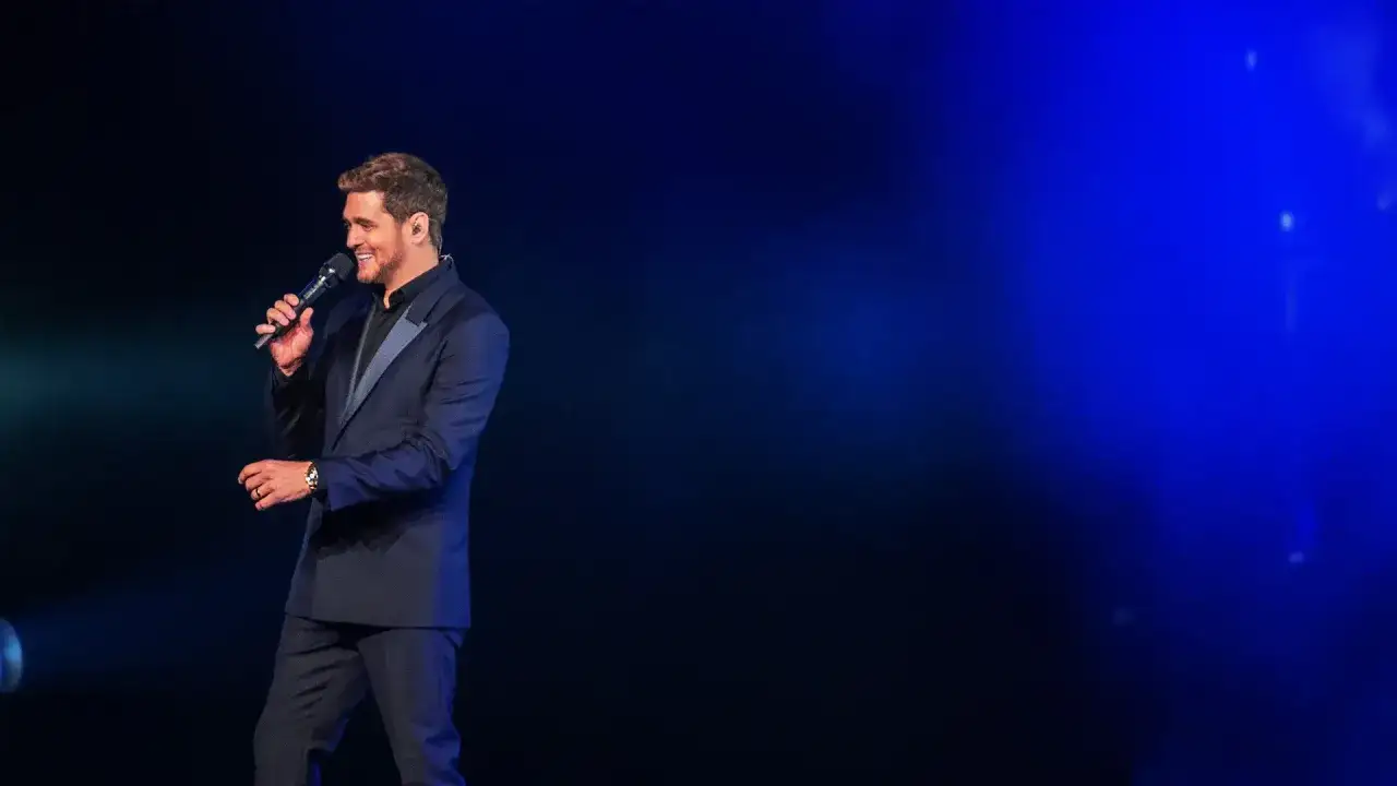 Michael Bublé śpiewa swoje utwory na scenie w eleganckim garniturze, oświetlony niebieskim światłem.