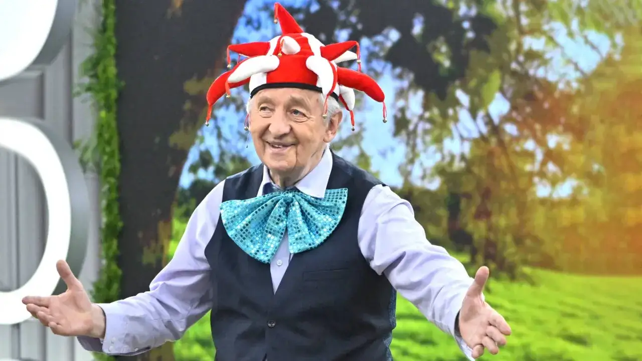 Uśmiechnięty starszy pan w czapce błazna i błyszczącej muszce. Może opowiada o swoich piosenkach Rosiewicza alfabetycznie?