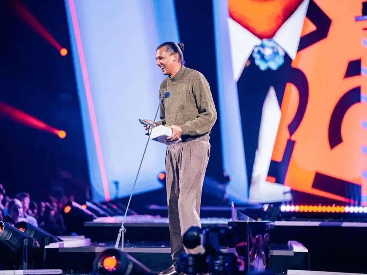 Stromae na scenie, odbiera nagrodę. W tle wielki ekran z grafiką przypominającą frak, jak w teledysku 